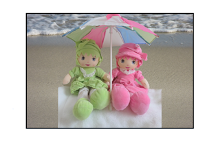 adorable dolls underneath an umbrella sitting on the beach