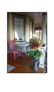 Porch with red wicker rocking chair, white wicker table and flower stand